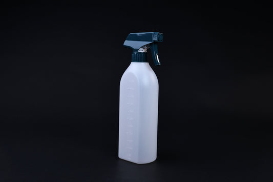 Flat-sided spray bottle standing upright on black background, teal trigger head and embossed volume markings