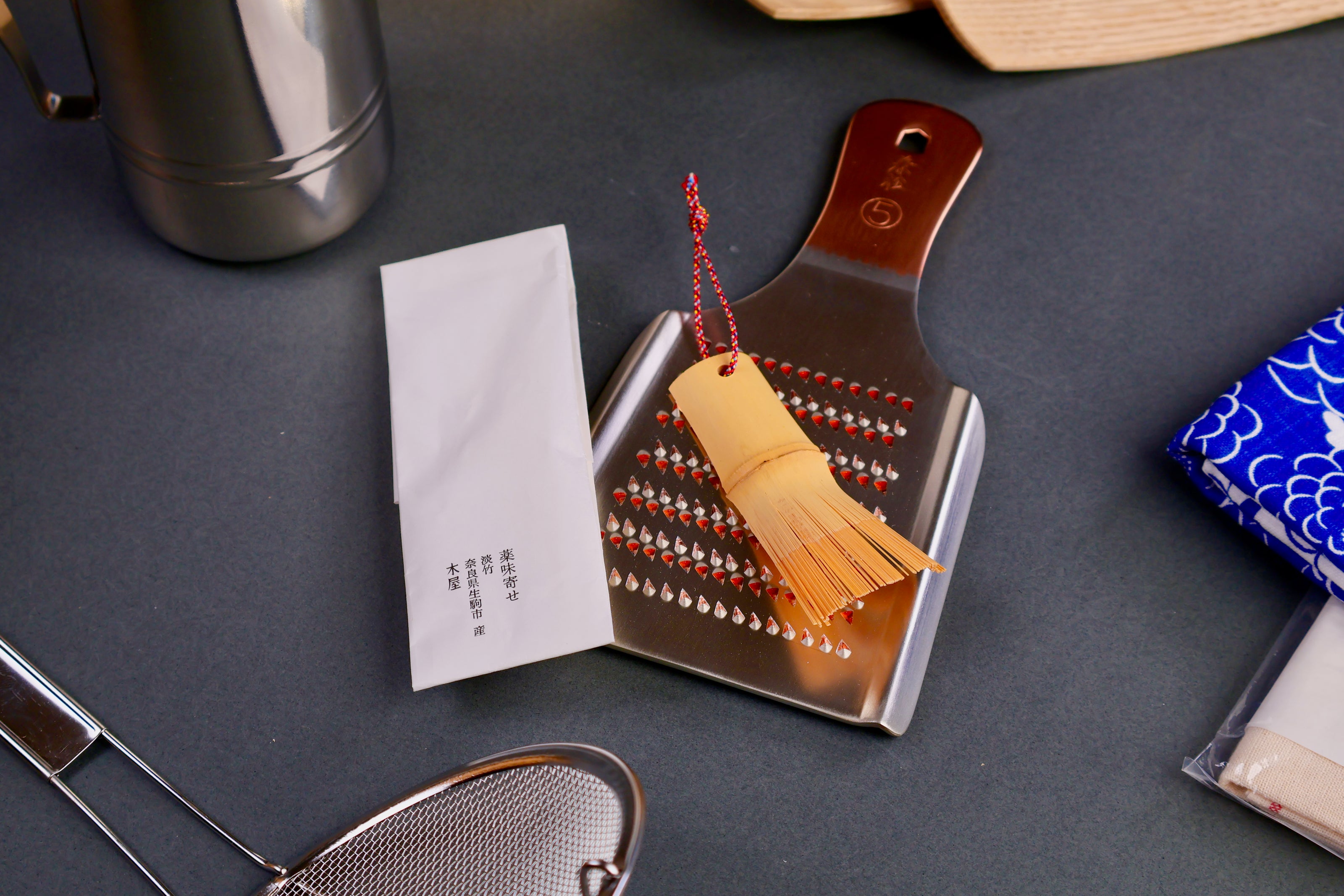 extra small bamboo chasen brush on top of oroshigane metal grater surrounded by kitchenware and grey backdrop