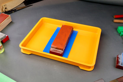 shot and wide yellow container holding hasegawa non slip mat and naniwa whetstone surrounded by knife accessories and grey backdrop
