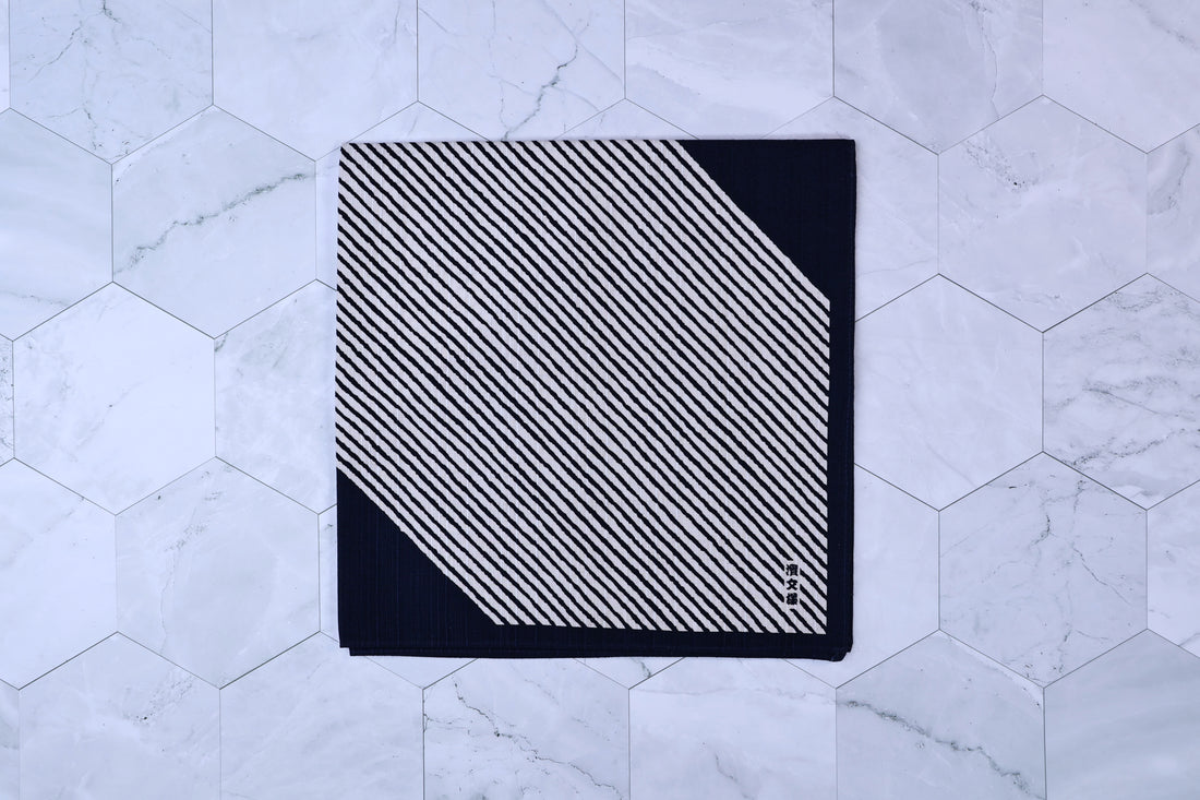 Hamamonyo classified stripes black tenugui folded on white hex tile, diagonal stripe pattern and Japanese mark visible