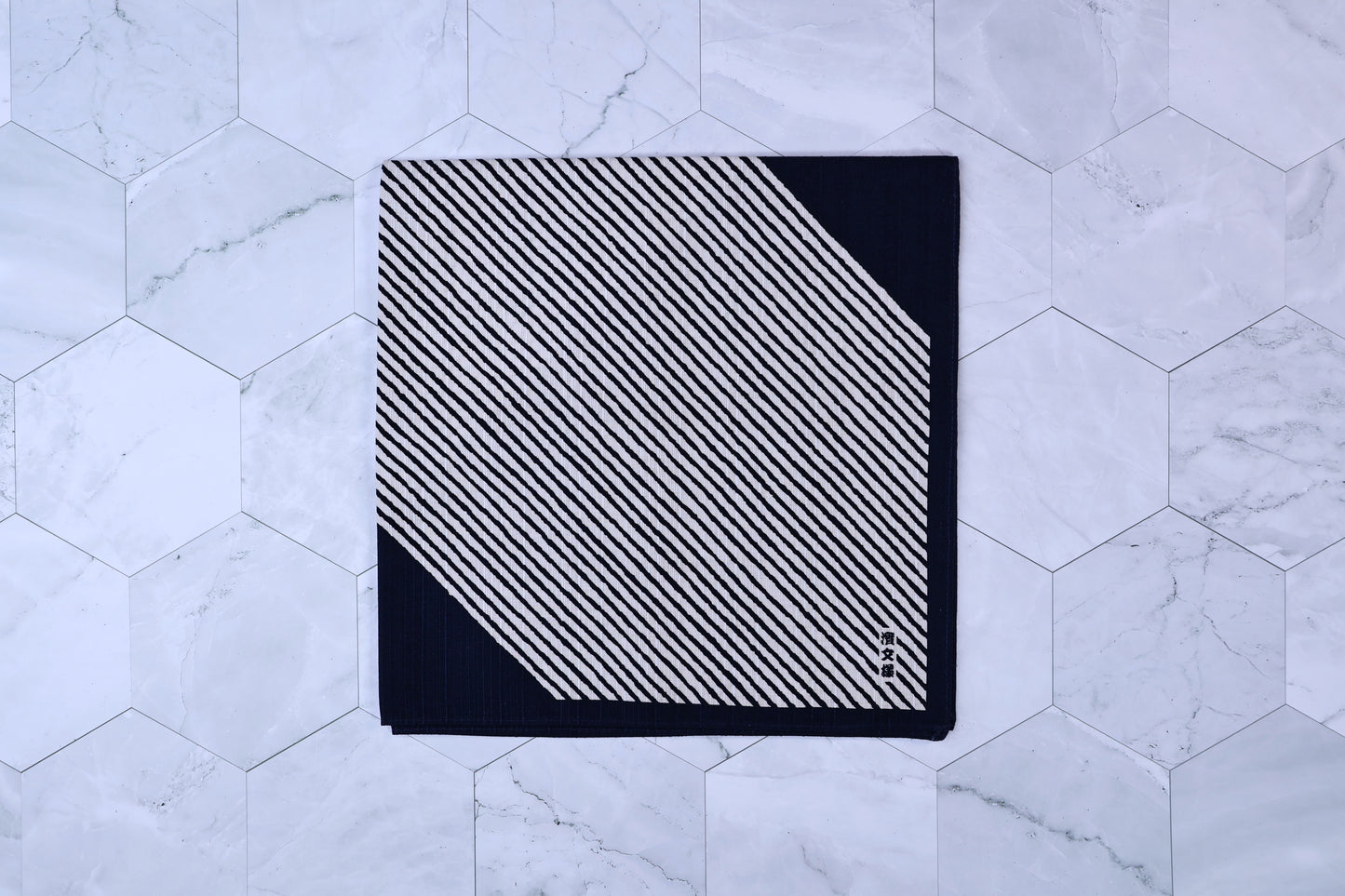 Hamamonyo classified stripes black tenugui folded on white hex tile, diagonal stripe pattern and Japanese mark visible