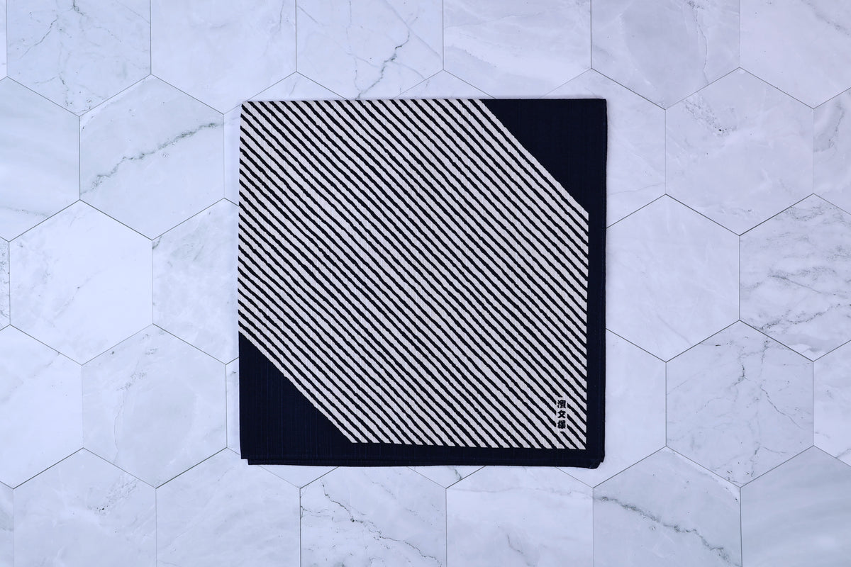 Hamamonyo classified stripes black tenugui folded on white hex tile, diagonal stripe pattern and Japanese mark visible