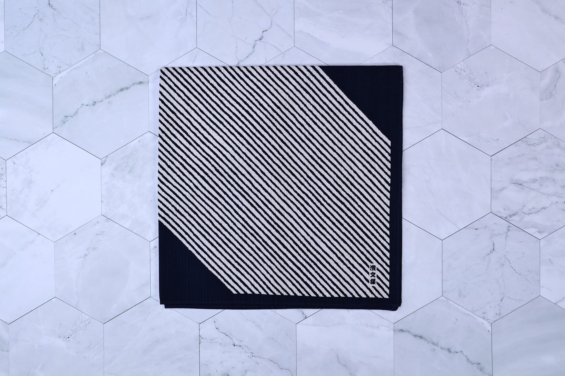 Hamamonyo classified stripes black tenugui folded on white hex tile, diagonal stripe pattern and Japanese mark visible