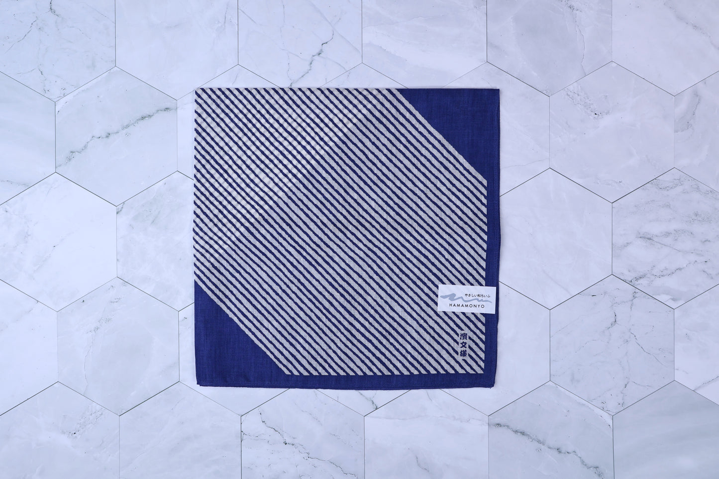 Hamamonyo classified stripes blue tenugui folded on white hex tile, diagonal stripe pattern and Hamamonyo label visible