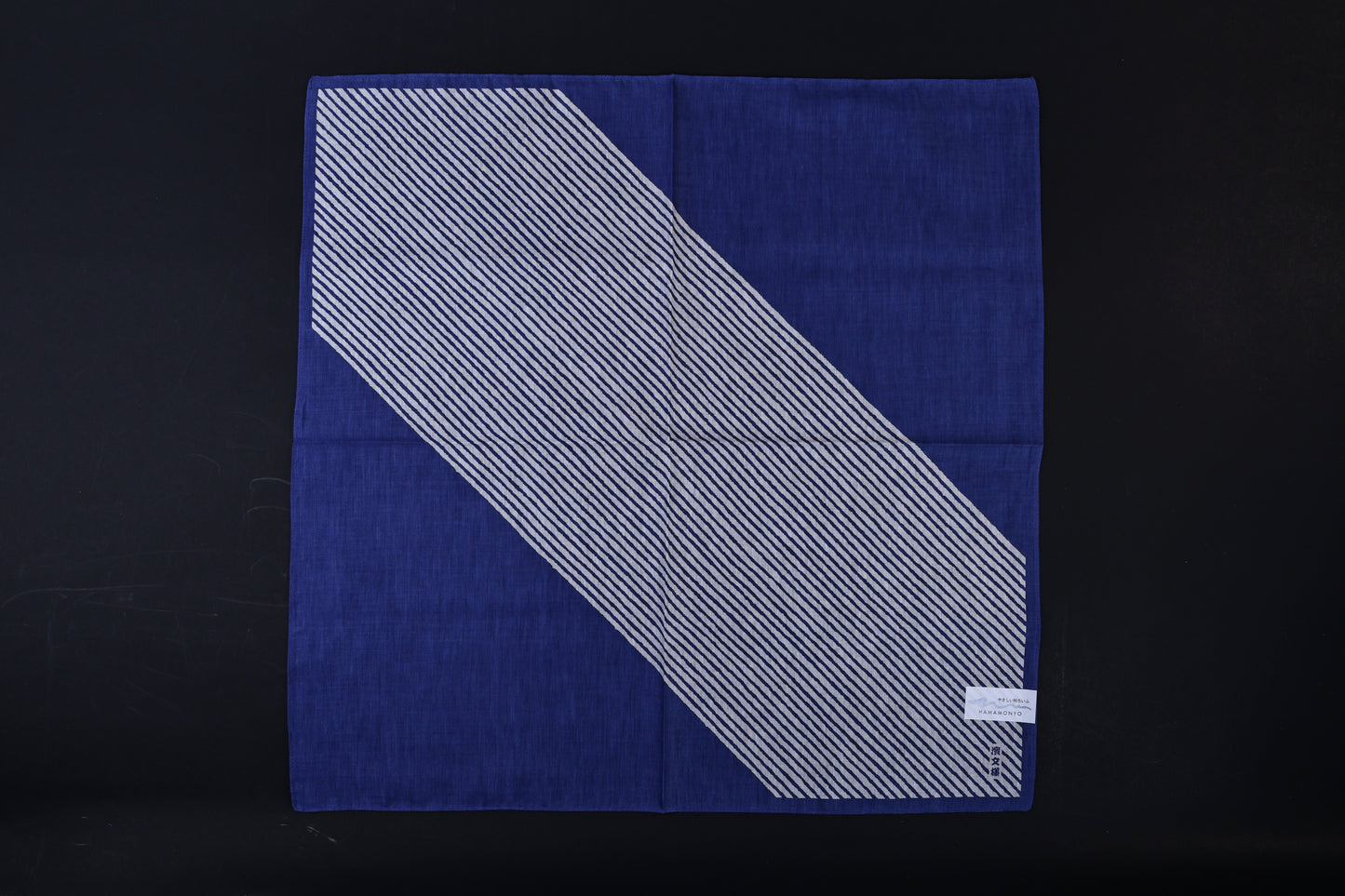 Hamamonyo classified stripes blue tenugui fully unfolded on black background, showing diagonal stripe design against solid blue