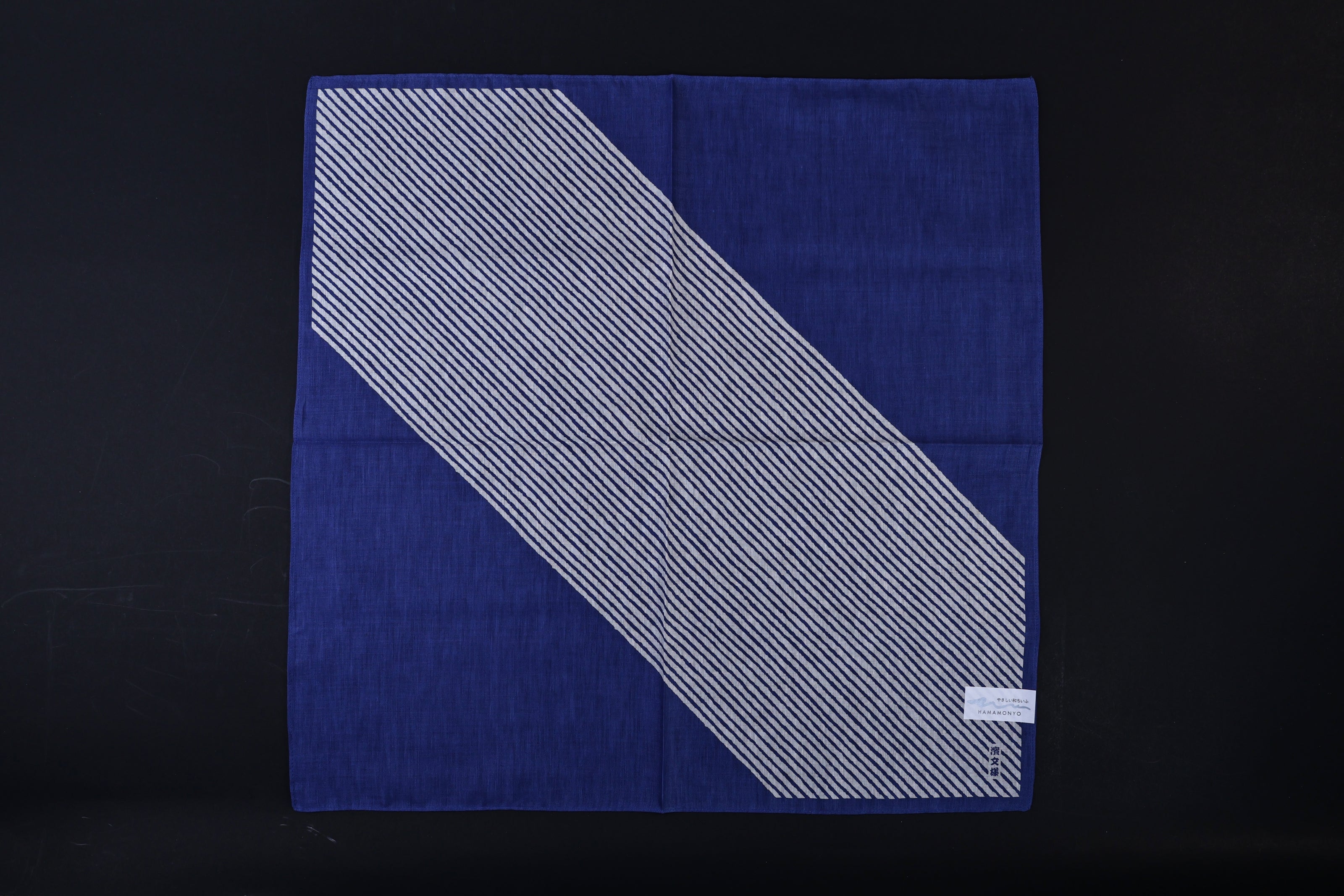 Hamamonyo classified stripes blue tenugui fully unfolded on black background, showing diagonal stripe design against solid blue