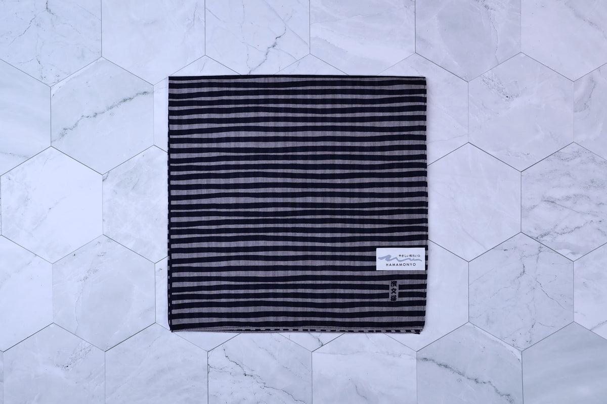 Hamamonyo tateyoko striped tenugui folded flat on white hex tile, Hamamonyo label visible in corner