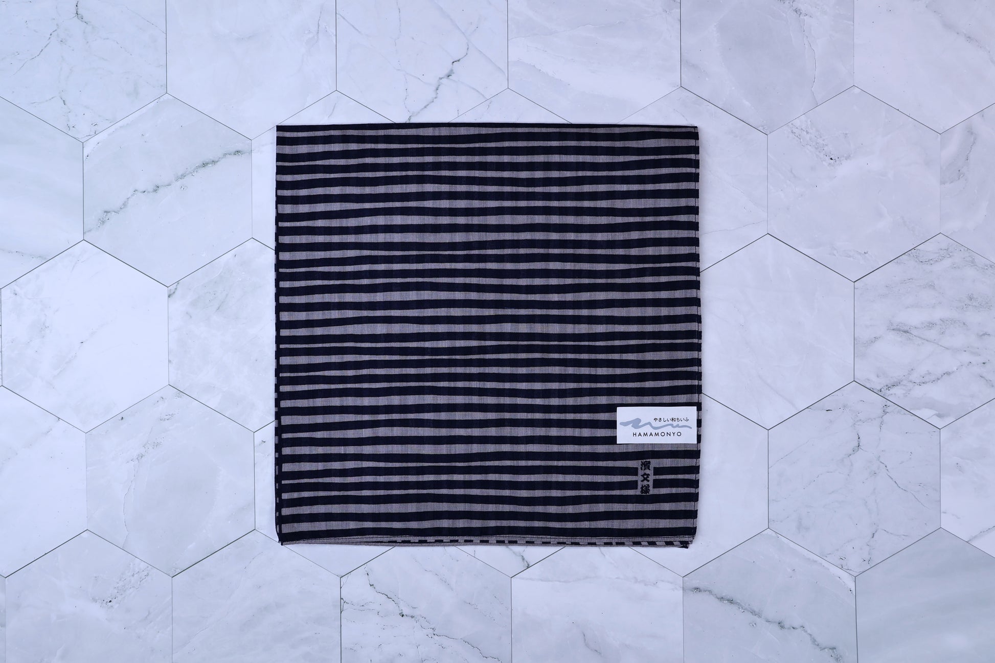 Hamamonyo tateyoko striped tenugui folded flat on white hex tile, Hamamonyo label visible in corner