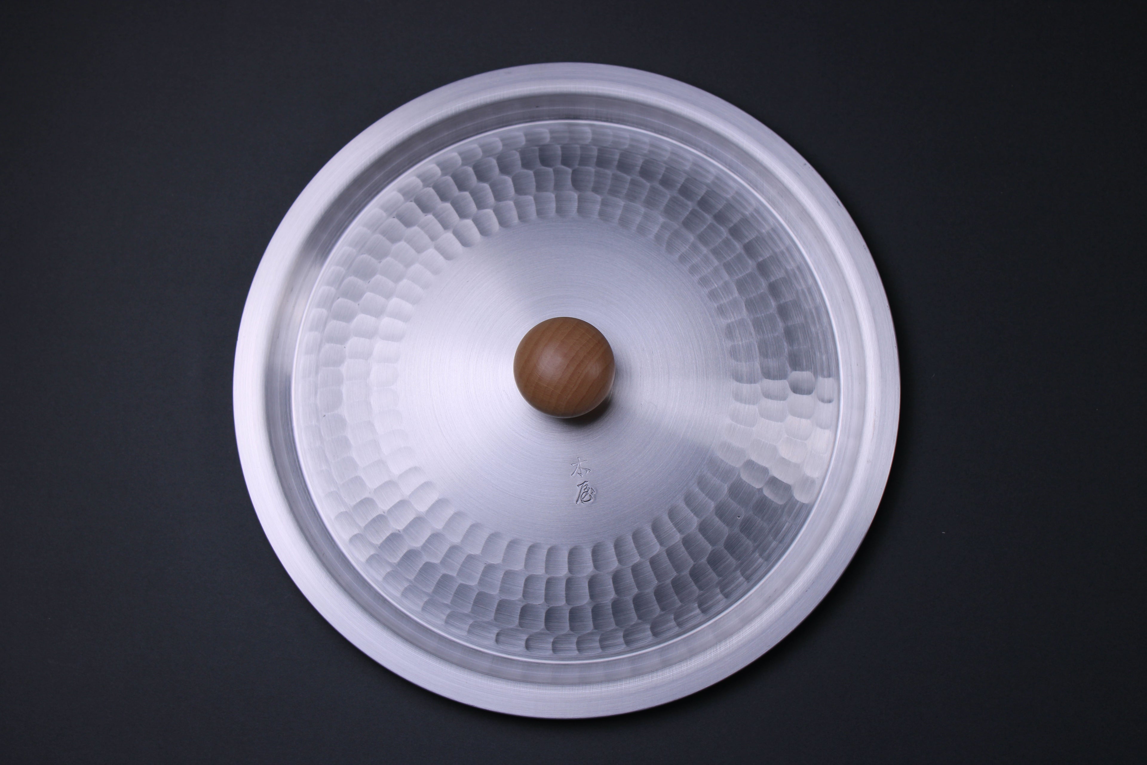 round metal lid hammered in center with kanji engraving small smooth wood knob in center dark background