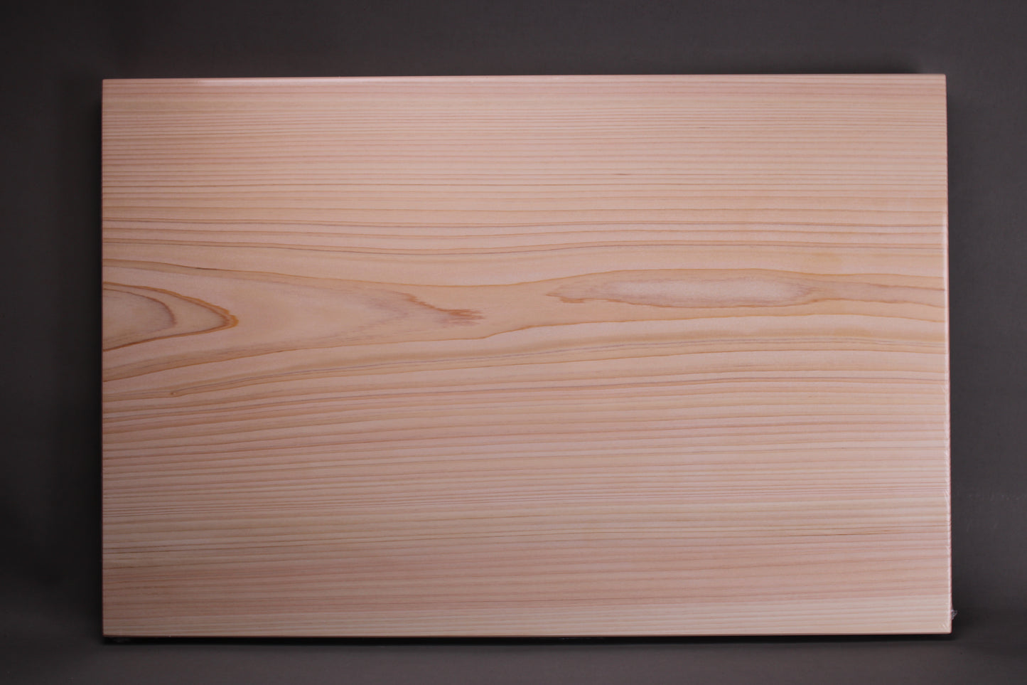 profile of solid piece straight grain yoshino hinoki wood cutting board with pinkish yellow and white hues of wood tone and soft even surface contrasted with dark grey black background