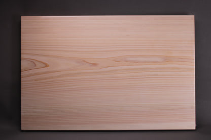 profile of solid piece straight grain yoshino hinoki wood cutting board with pinkish yellow and white hues of wood tone and soft even surface contrasted with dark grey black background