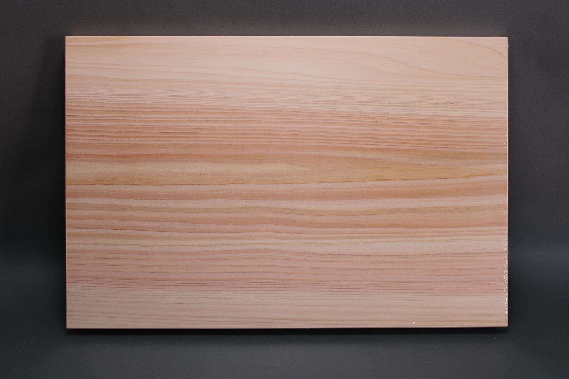 rectangular shaped light medium deep wood tan hinoki cutting board with deep natural grain lines in front of dark grey backdrop