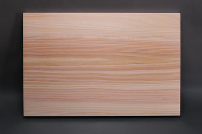 rectangular shaped light medium deep wood tan hinoki cutting board with deep natural grain lines in front of dark grey backdrop