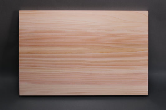 rectangular shaped light medium deep wood tan hinoki cutting board with deep natural grain lines in front of dark grey backdrop