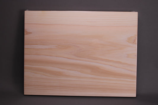 rectangular shaped light medium deep wood tan hinoki cutting board with deep natural grain lines in front of dark grey backdrop