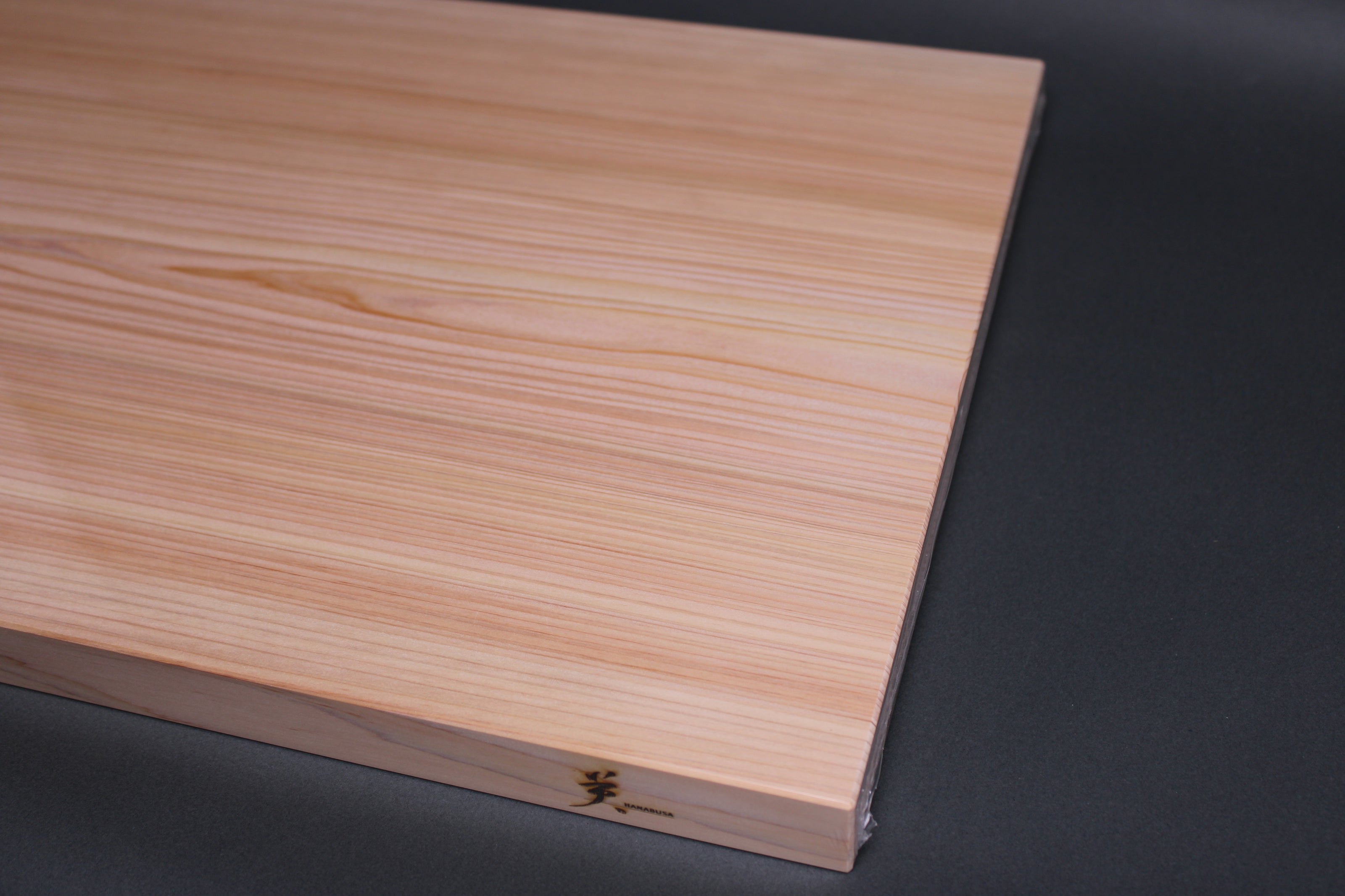 close up end rectangular shaped light medium deep wood tan hinoki cutting board with deep natural grain lines in front of dark grey backdrop