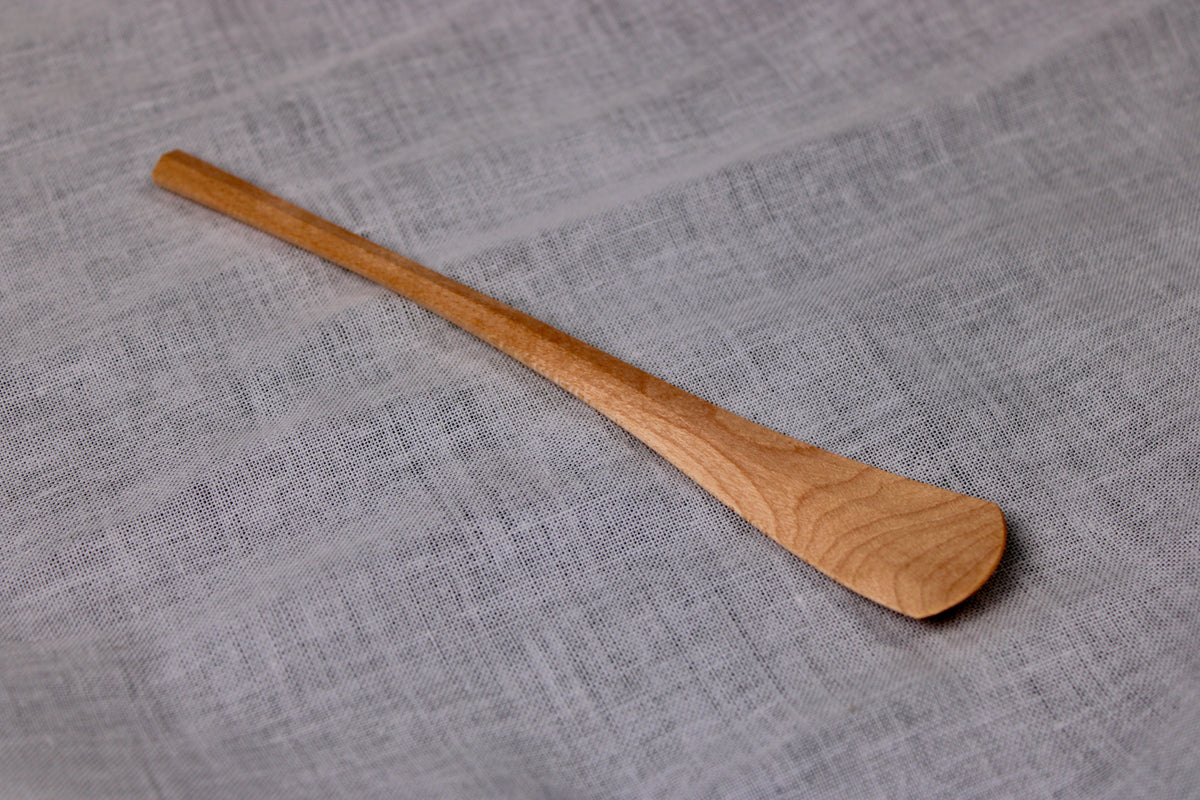 long thin wooden tan jam spoon showing wood grain on white cloth background