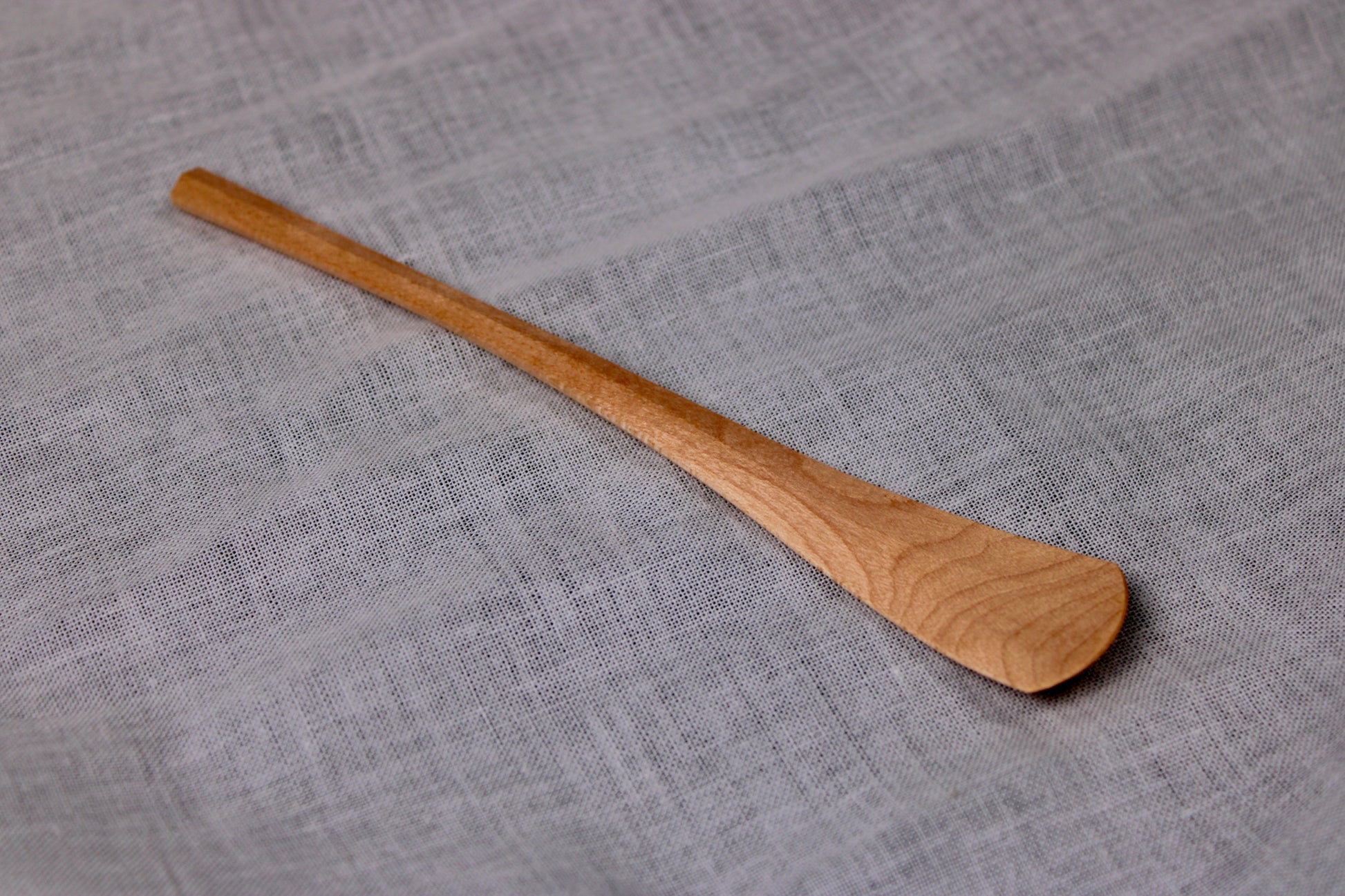 long thin wooden tan jam spoon showing wood grain on white cloth background