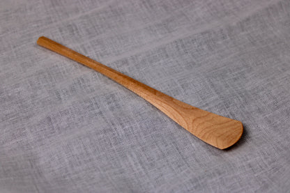 long thin wooden tan jam spoon showing wood grain on white cloth background