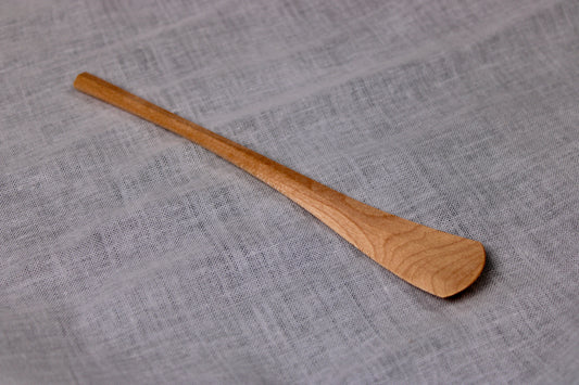 long thin wooden tan jam spoon showing wood grain on white cloth background