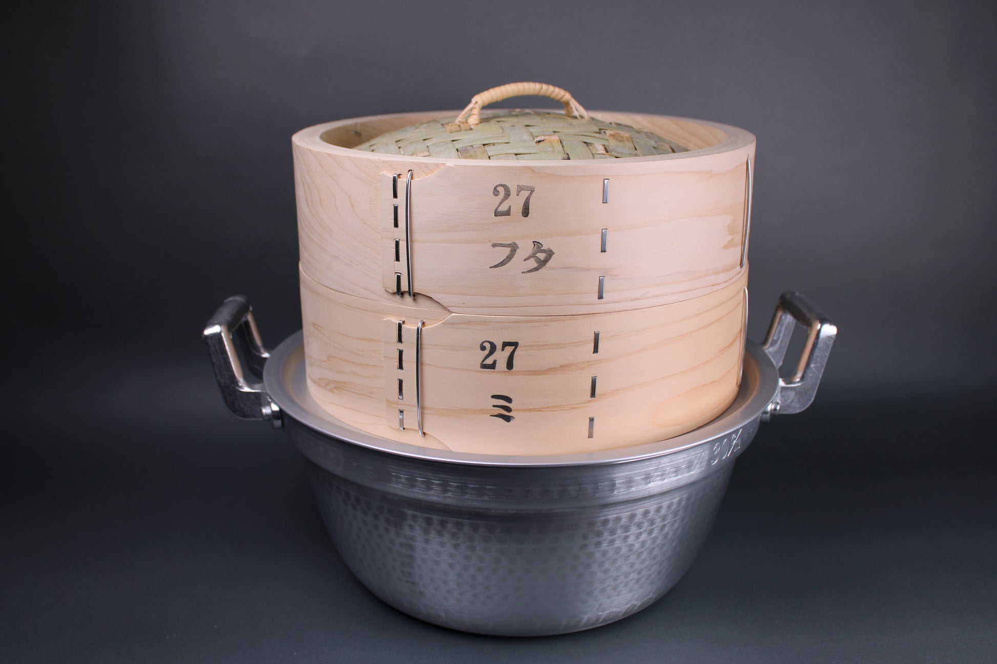 profile shot of Hiko and bamboo steamer kit with lid and base of steamer sitting on japanese steaming pot and ring which fits perfectly surrounding a dark gray background 