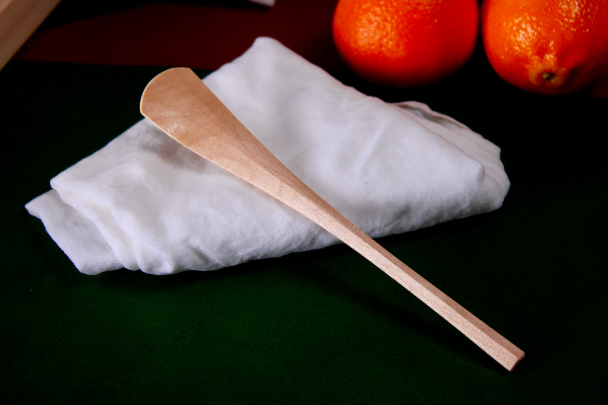 long thin wooden tan jam spoon showing wood grain on white cloth background with oranges 