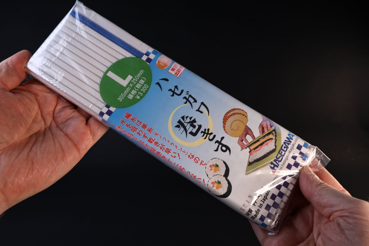 Hasegawa white antibacterial sushi rolling mat in size L packaging, held front side out against a dark background