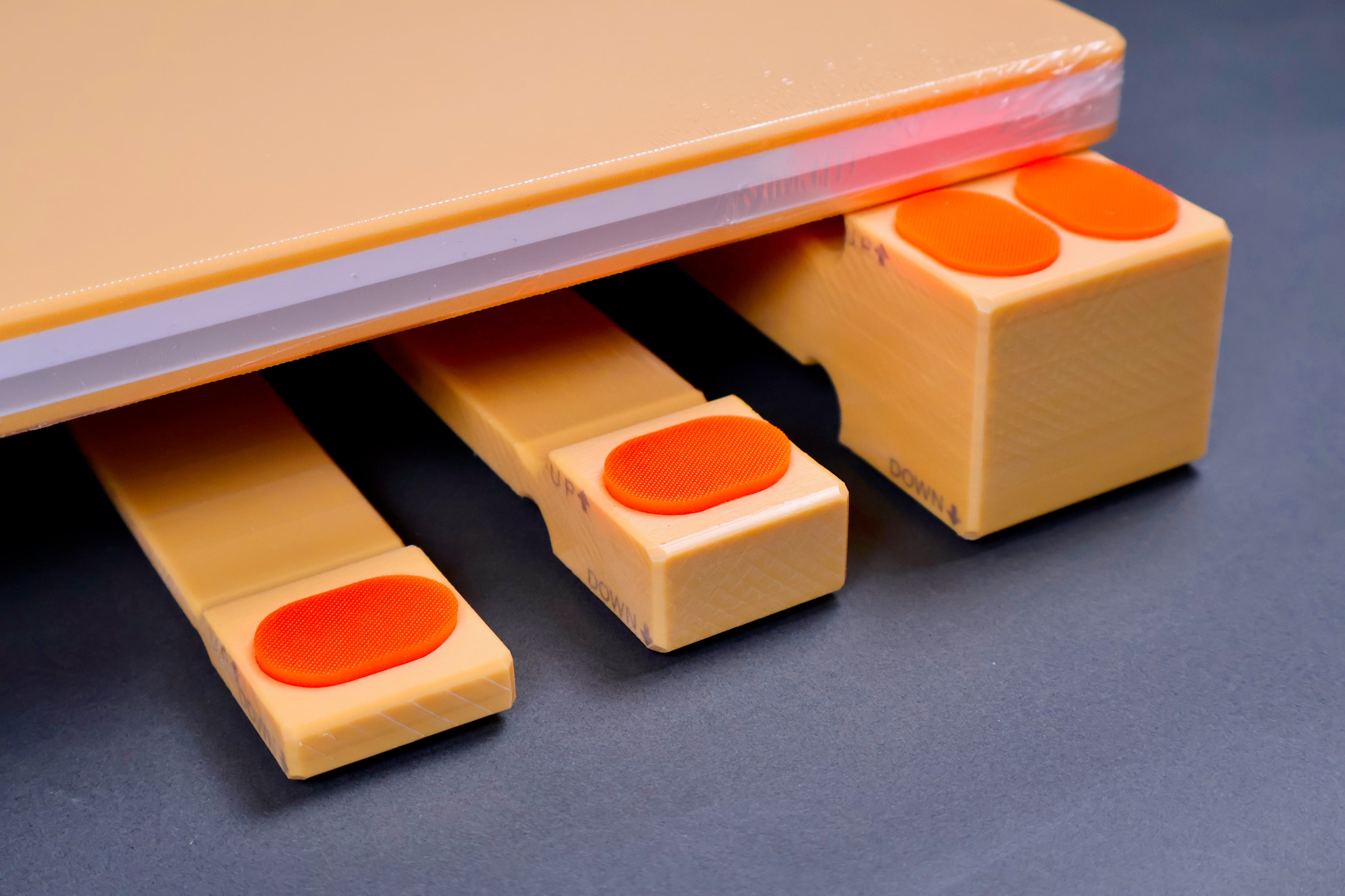 three sizes of hasegawa cutting board lifters long rectangular shaped with pill shaped bright orange oval non slip material in blue grey background