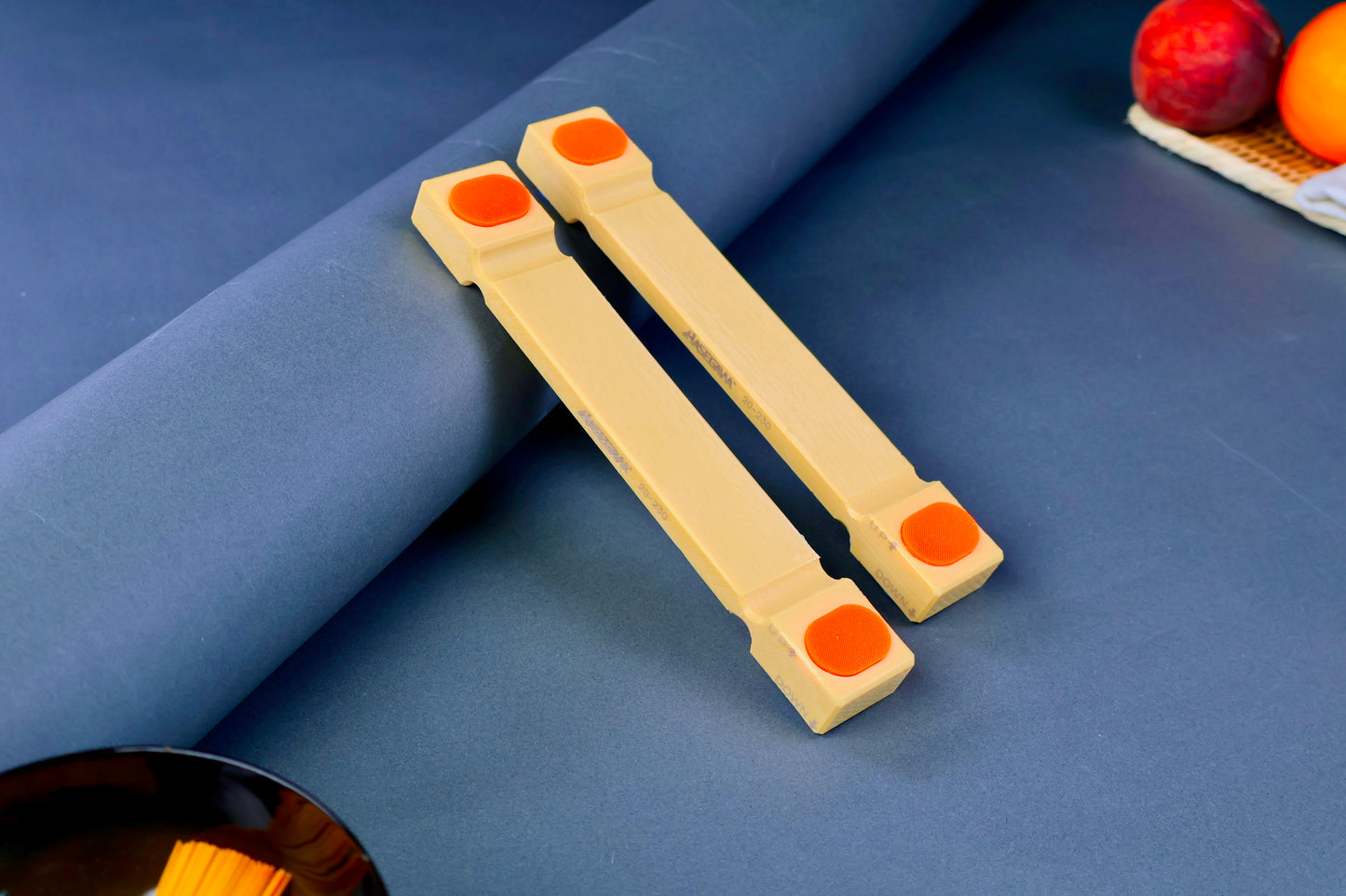 hasegawa cutting board lifter twenty mm tall long rectangular shaped with pill shaped bright orange oval non slip material in blue grey background with fruit and towel 