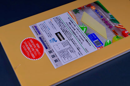 detail of long yellow rectangular shaped rubber cutting board with product paper in hiragana showing bright green red blue images surrounded by kitchenware on grey background