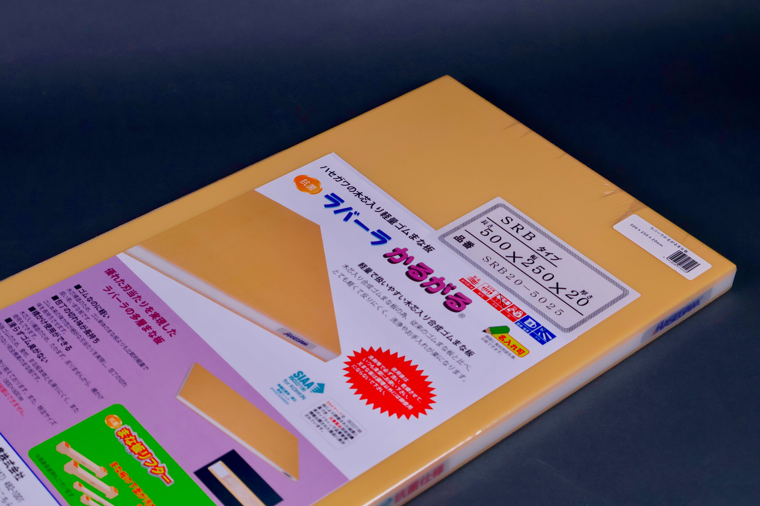 detail of long yellow rectangular shaped rubber cutting board with product paper in hiragana showing bright green red blue images surrounded by kitchenware on grey background