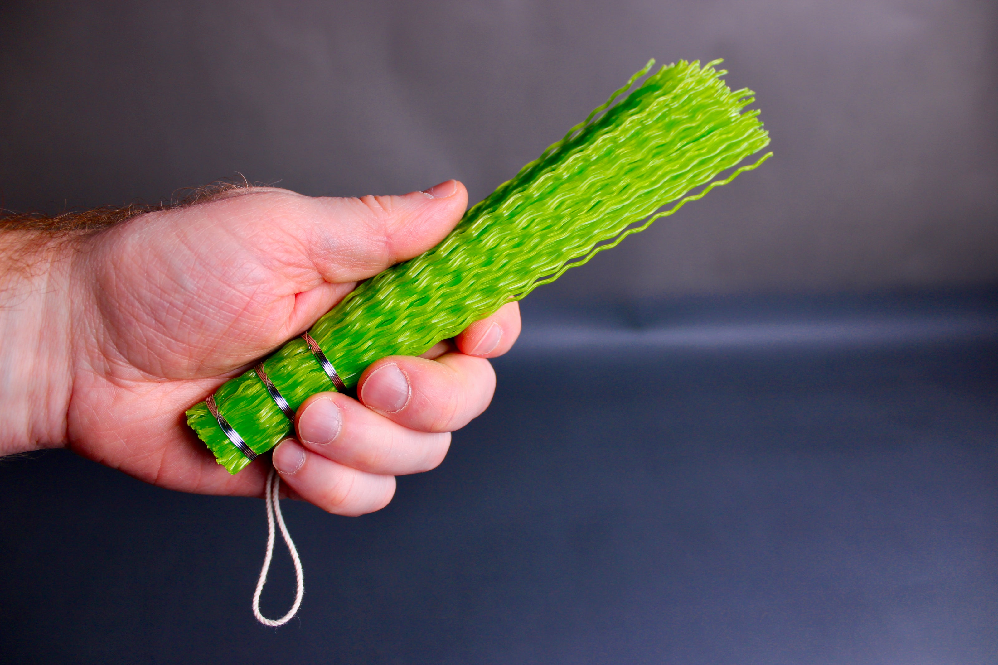 hand holding green brush with white loop string grey background