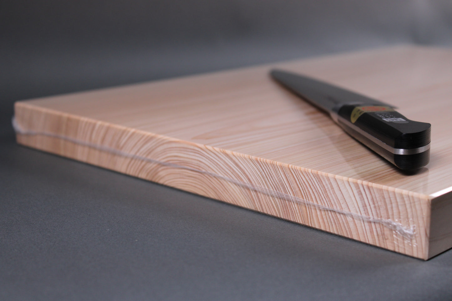up close shot of side of cutting board showing even layers of tree rings throughout the entire board with black handled jikko knife atop with dark gray background 