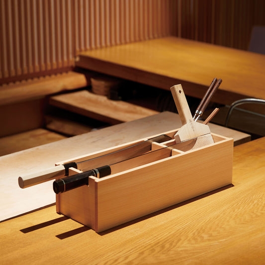 hinoki wood rectangular shaped box with natural wood grain sits atop wood counter surrounding japanese restaurant background