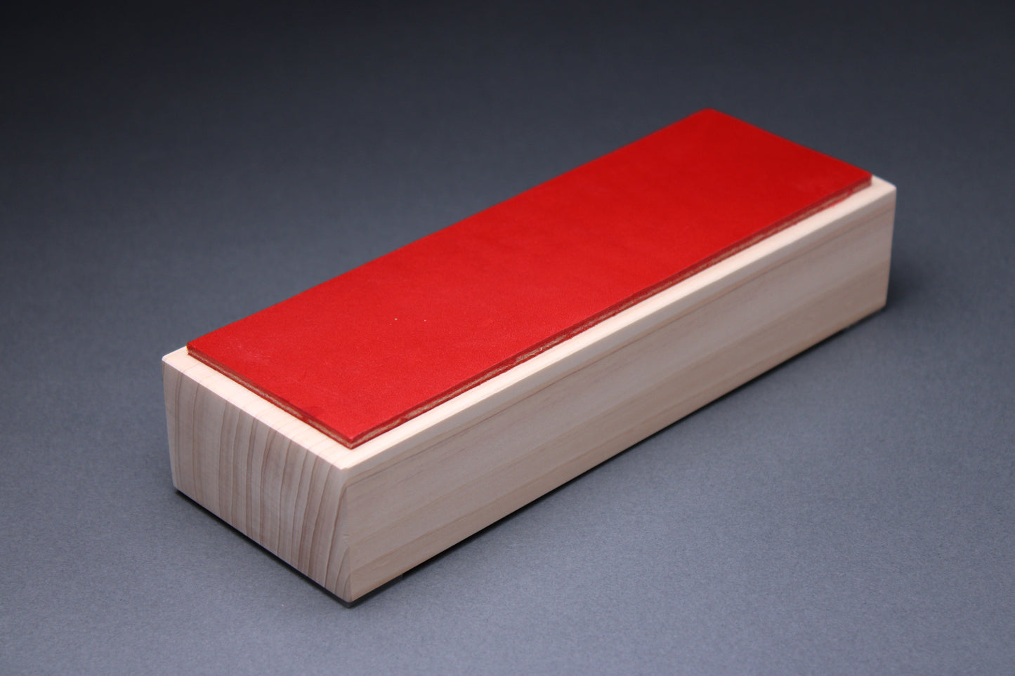 Hinoki vermilion leather knife strop — three-quarter view showing red leather surface on hinoki wood base