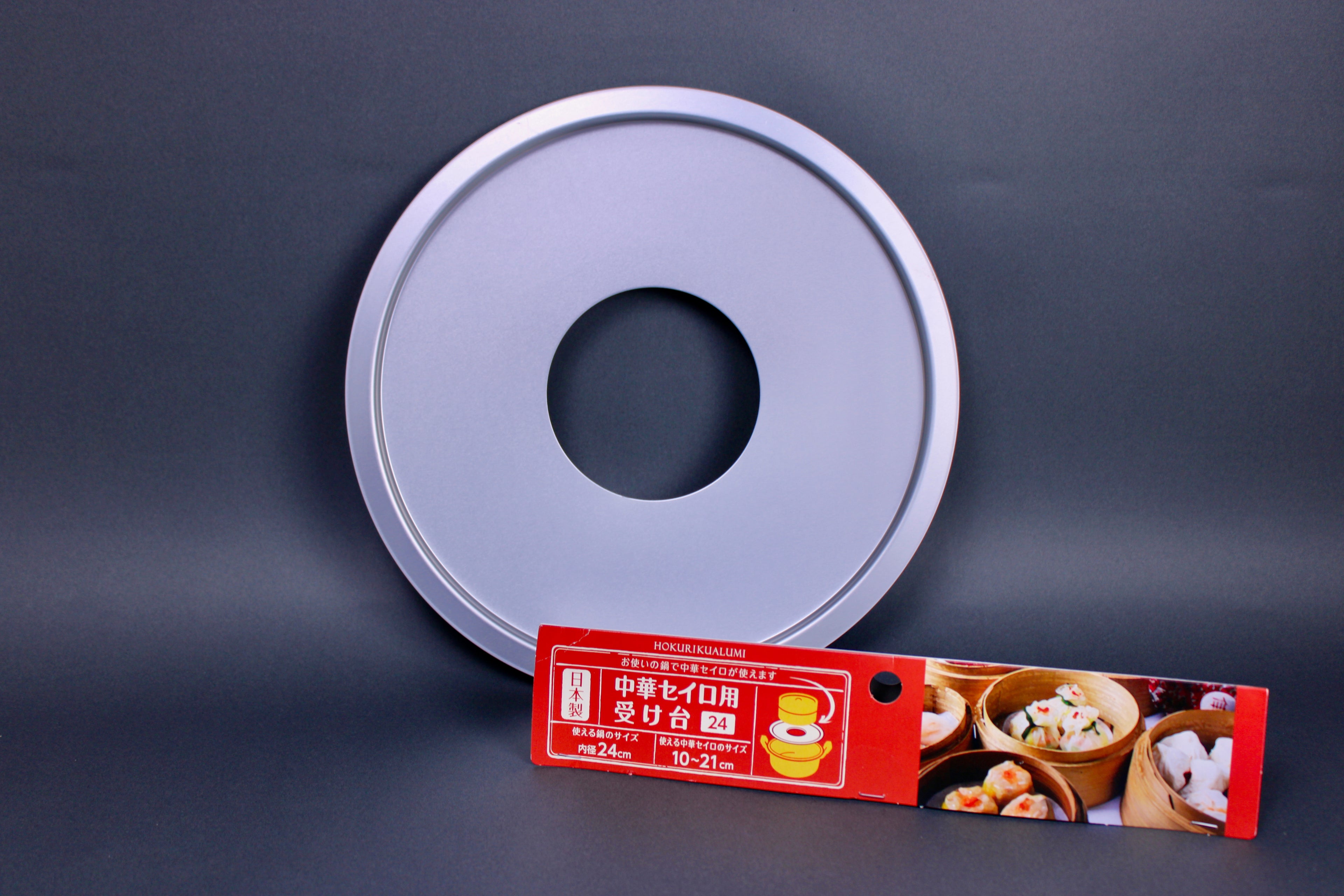 metalic shiny circular steam ring for bamboo steamer center hole next to red yellow white product card showing steamed food dark grey background