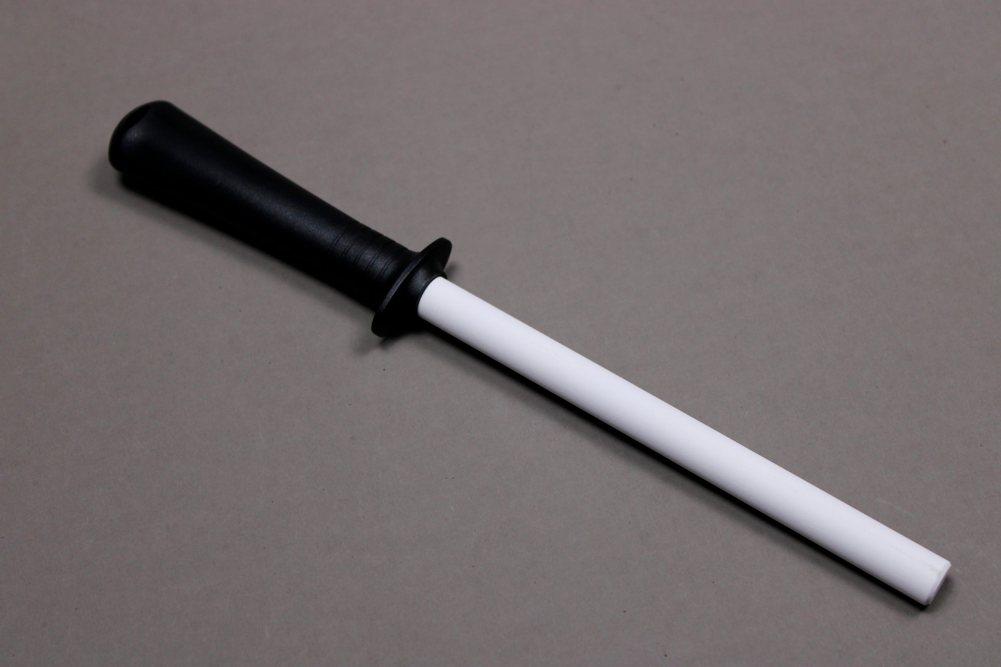 plastic black handled white ceramic honing rod angled on grey background