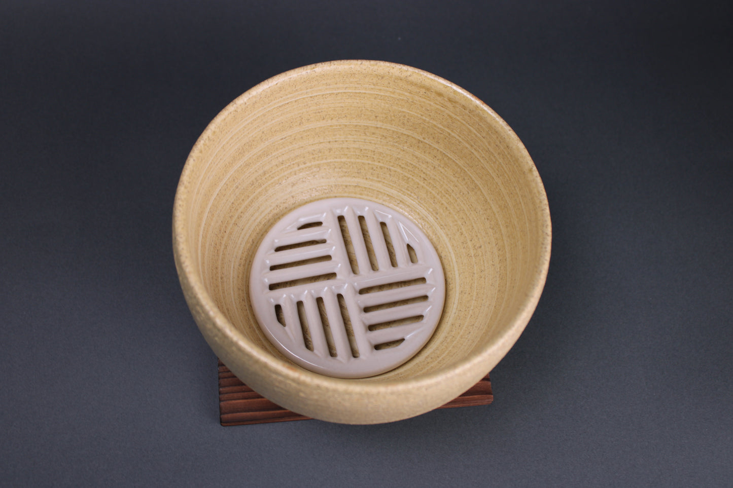 top down image showing the details of the earthenware vessel with a ceramic grate at the bottom for steaming food the product sits on a textured deep brown square piece of wood used as a trivet surrounded with a grey backdrop