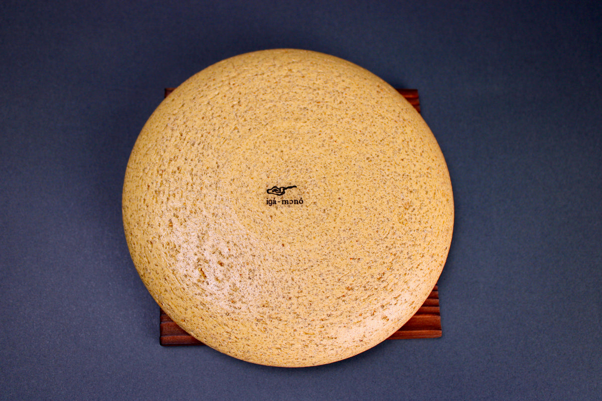 round yellowish ceramic lid sitting atop tan wood trivet in grey background