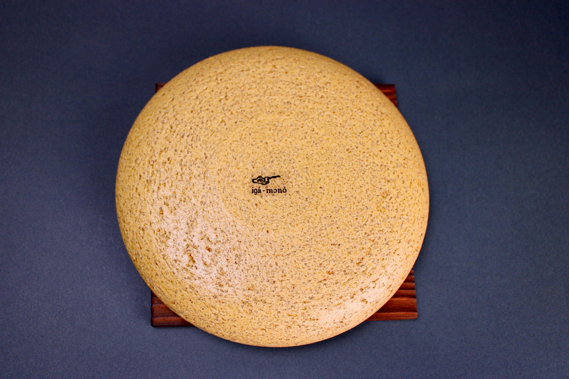 round yellowish ceramic lid sitting atop tan wood trivet in grey background