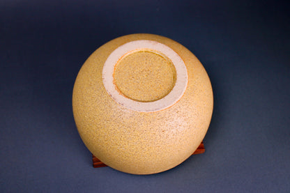 round yellowish ceramic bowl underside sitting atop tan square wooden trivet in grey background