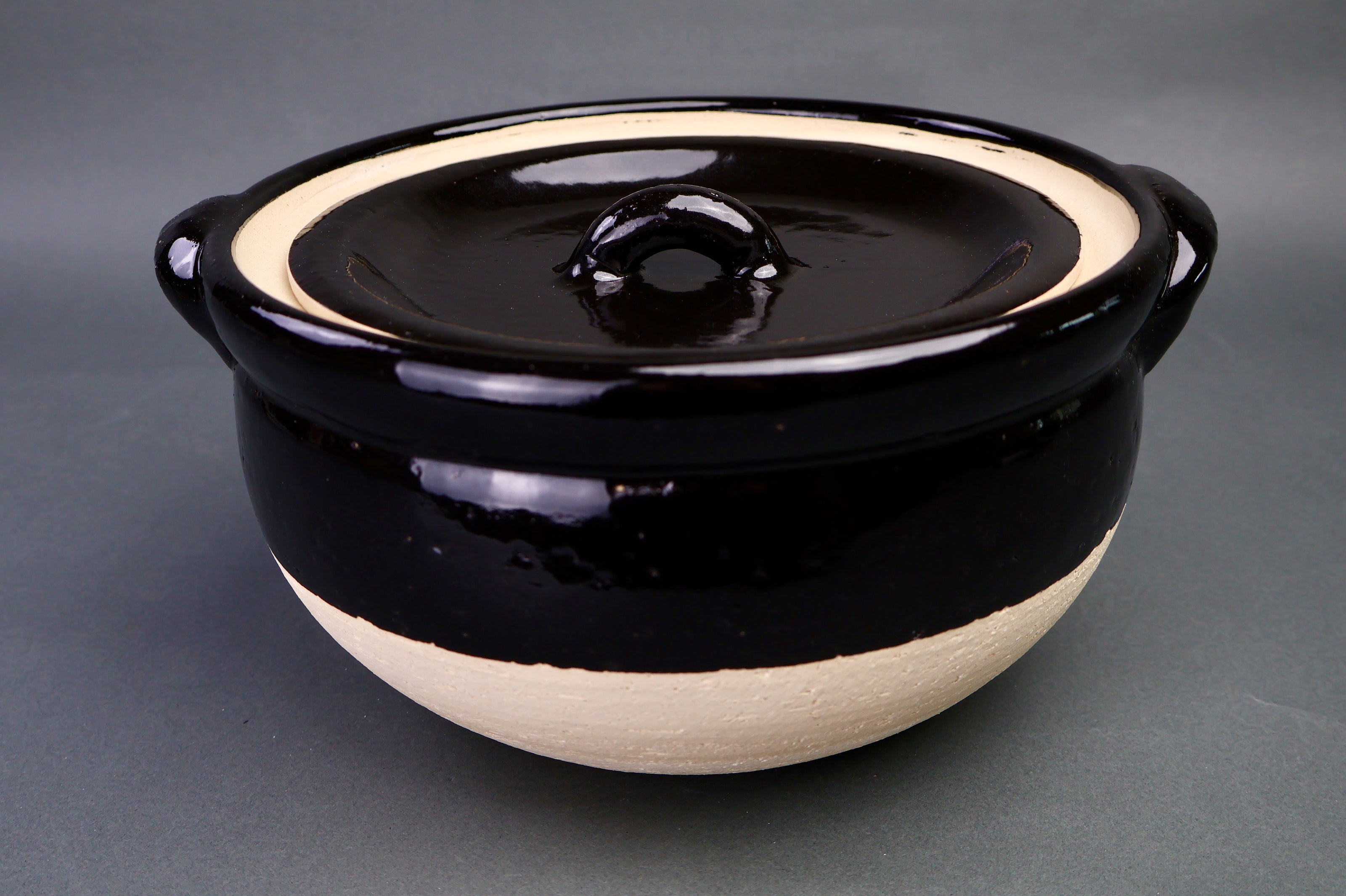 black glazed ceramic rice donabe with two lids surrounded by grey background