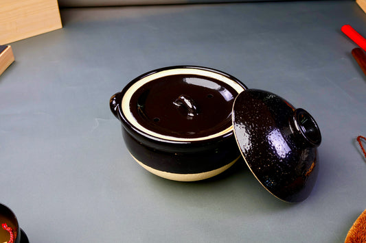 black glazed ceramic rice donabe with two lids surrounded by grey background