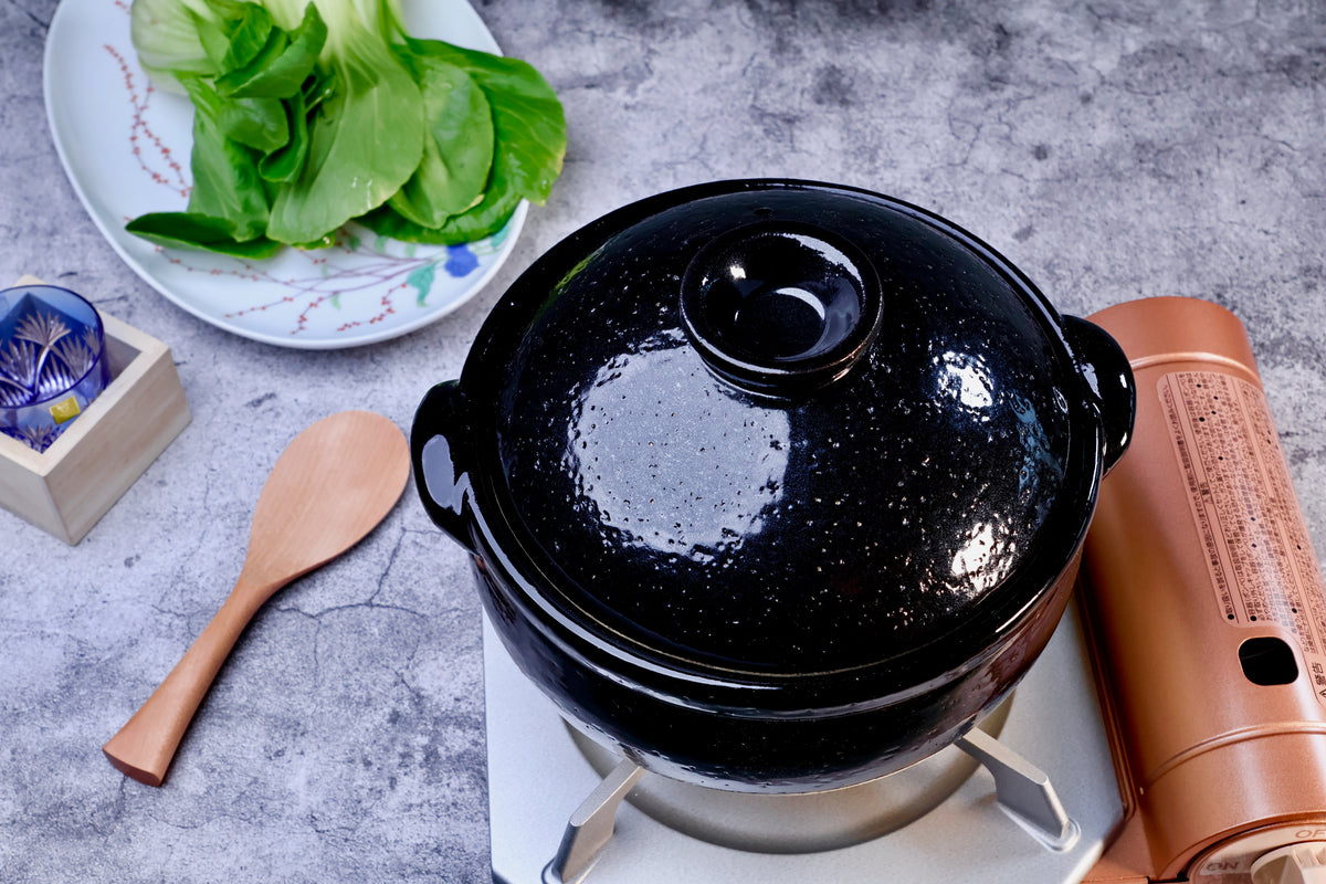 Iga Yaki rice donabe on portable gas burner, black glazed lid with speckled finish, styled with greens and sake