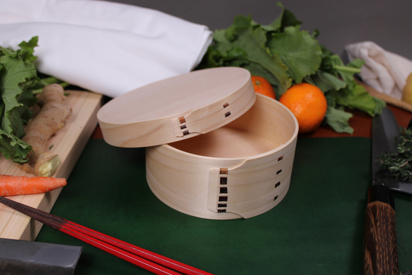 close up of hinoki cypress ohitsu rice tub lid askew beside japanese cookware tangerines sarashi