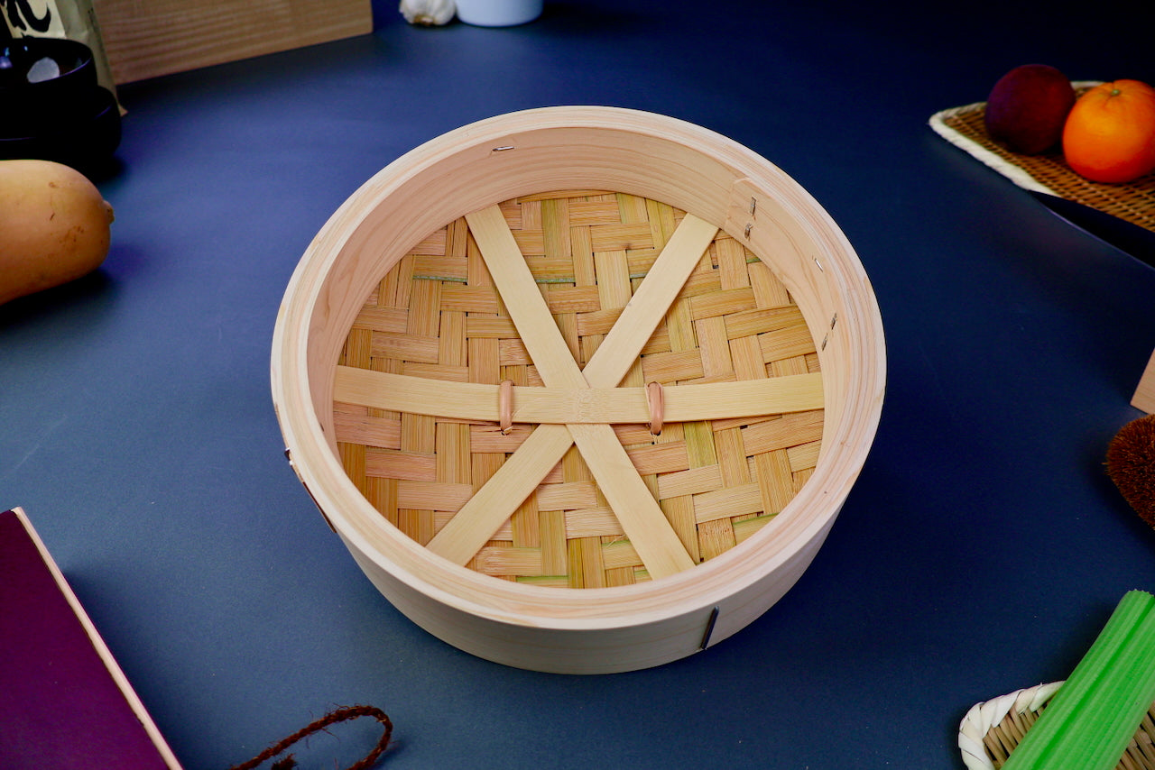round thick lid of bamboo steamer interior showing three support slats and woven bamboo top surrounded by kitchenware on blue gray surface