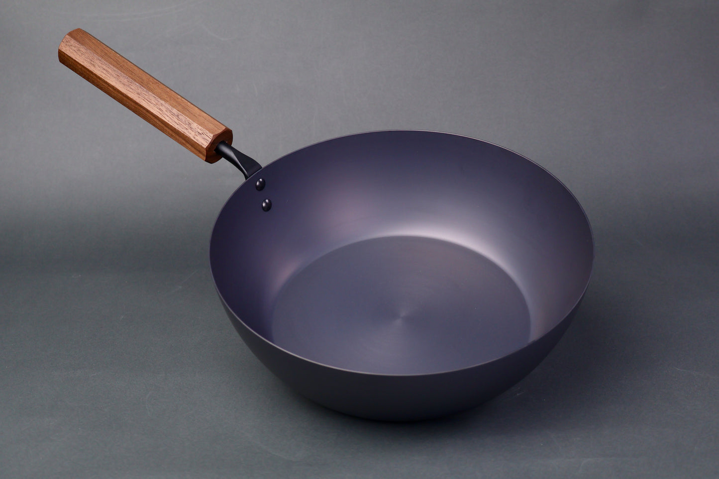 wide deep bluish black carbon steel pan long octagonal wood handle in light grey backdrop