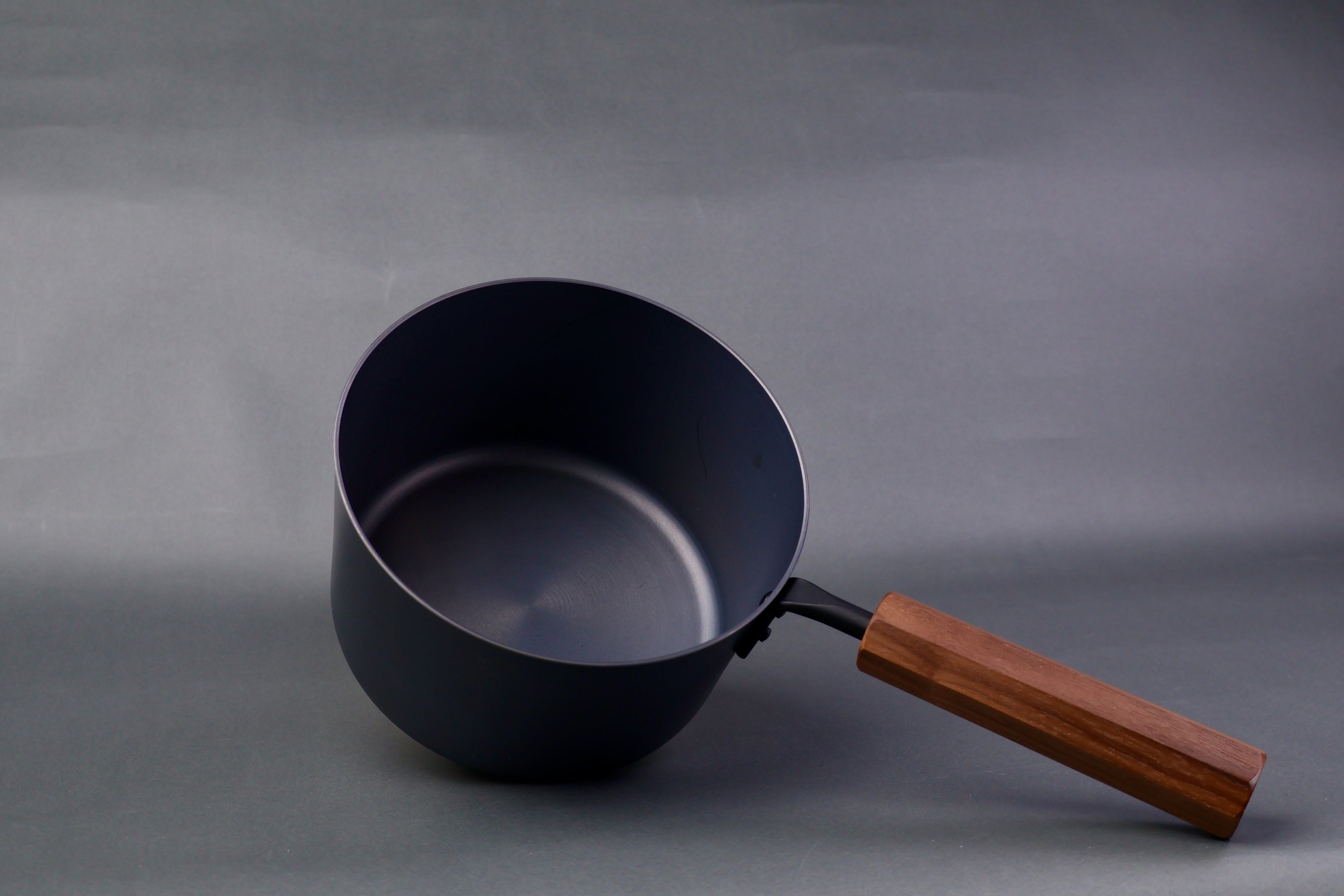 dark grey carbon steel tall narrow iron saucepan with octagonal deep brown wood handle in light grey background