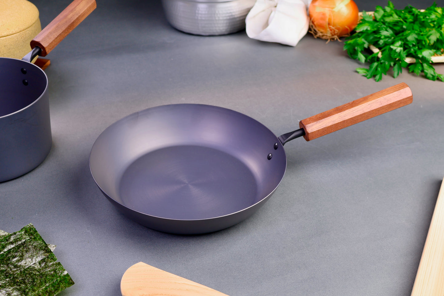 closeup shot of iron pan with wood handle surrounded by Japanese kitchenware with light grey background