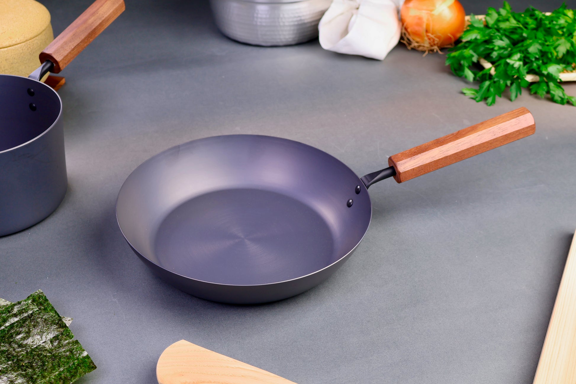 closeup shot of iron pan with wood handle surrounded by Japanese kitchenware with light grey background